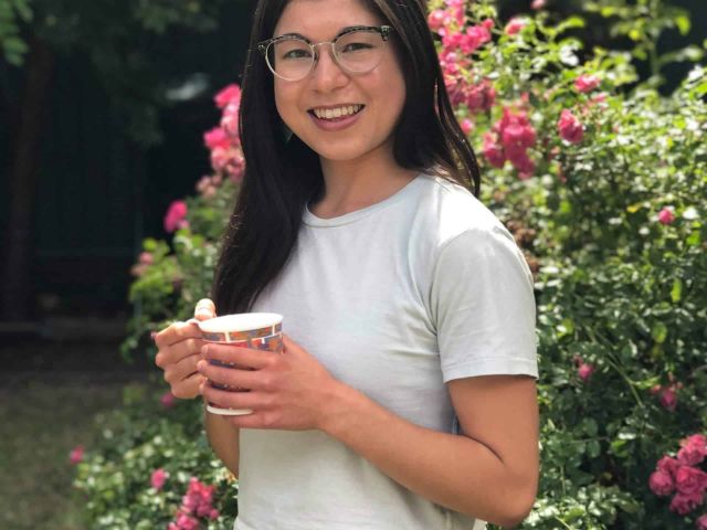 meg lee smiling holding a cup of cofee in a garden